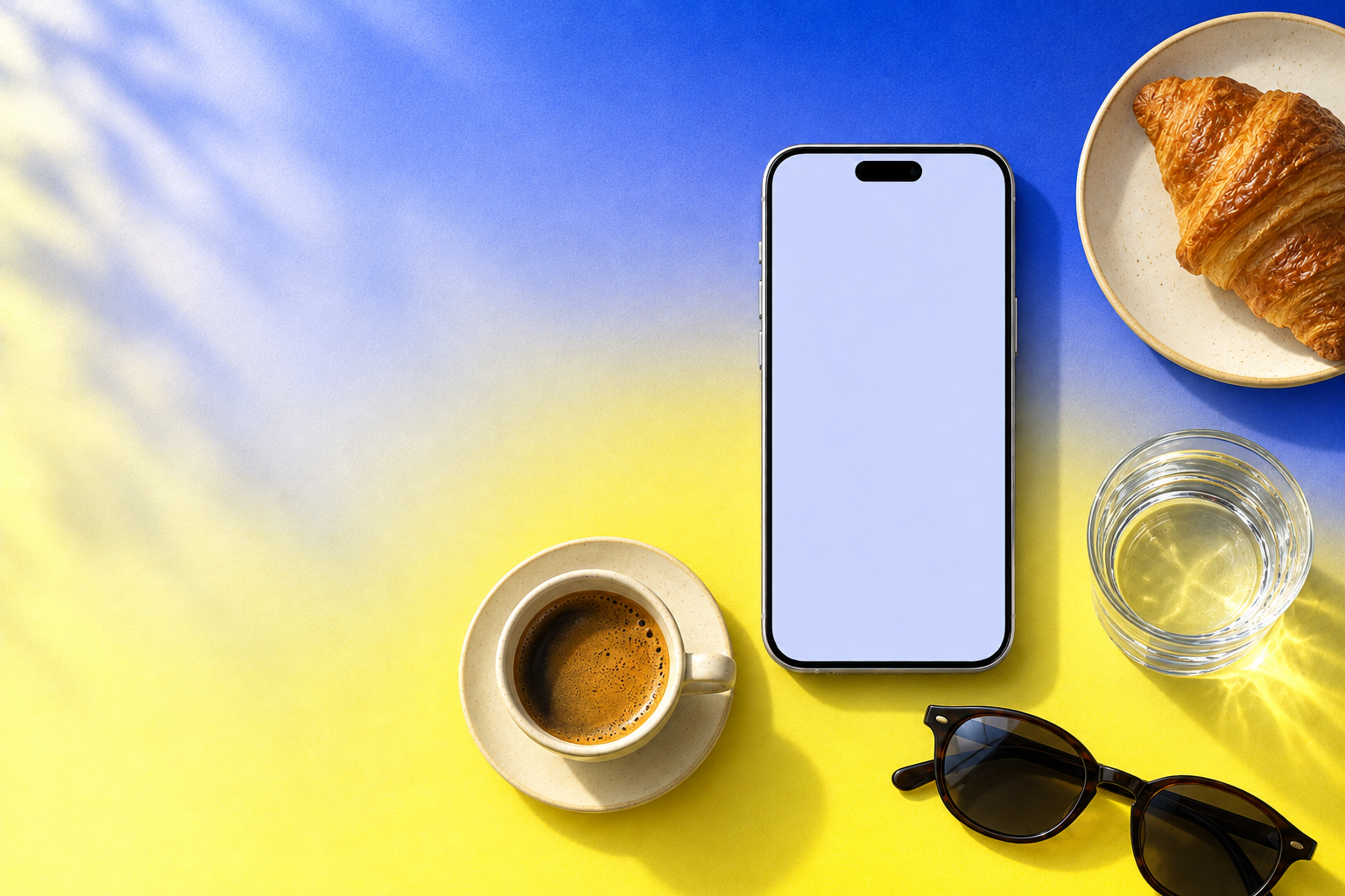 A blue and yellow still life with a phone, coffee, a croissant, water and sunglasses